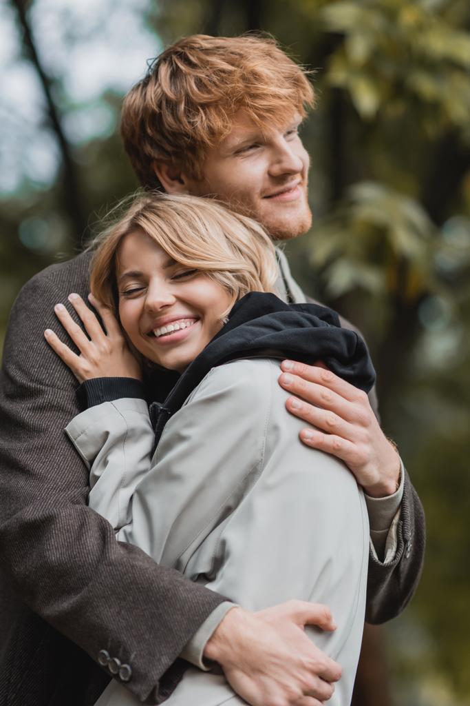 pareja alegre y joven en abrigos otoñales abrazándose entre sí durante la fecha - Foto, imagen