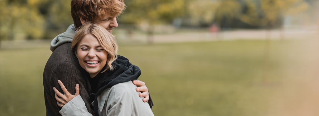 Sonbahar paltolu neşeli adam ve kadın parkta buluşurken birbirlerine sarılıyorlar. - Fotoğraf, Görsel
