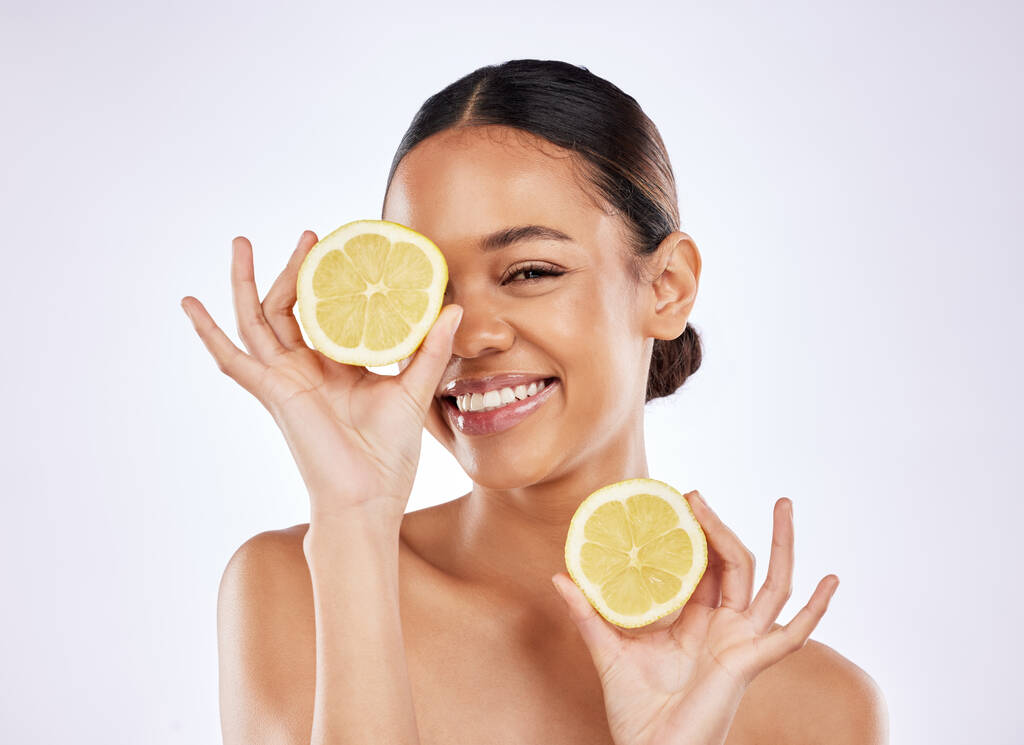 Один лимон от чистой кожи. красивая молодая женщина закрывает глаза лимоном на фоне студии - Фото, изображение
