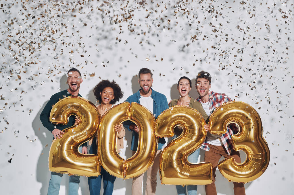 Groep van jonge mooie mensen in casual kleding dragen goud gekleurde nummers en glimlachen terwijl staan tegen grijze achtergrond - Foto, afbeelding