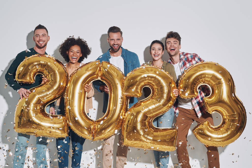 Gruppe junger schöner Menschen in lässiger Kleidung mit goldfarbenen Zahlen und lächelnd vor grauem Hintergrund - Foto, Bild