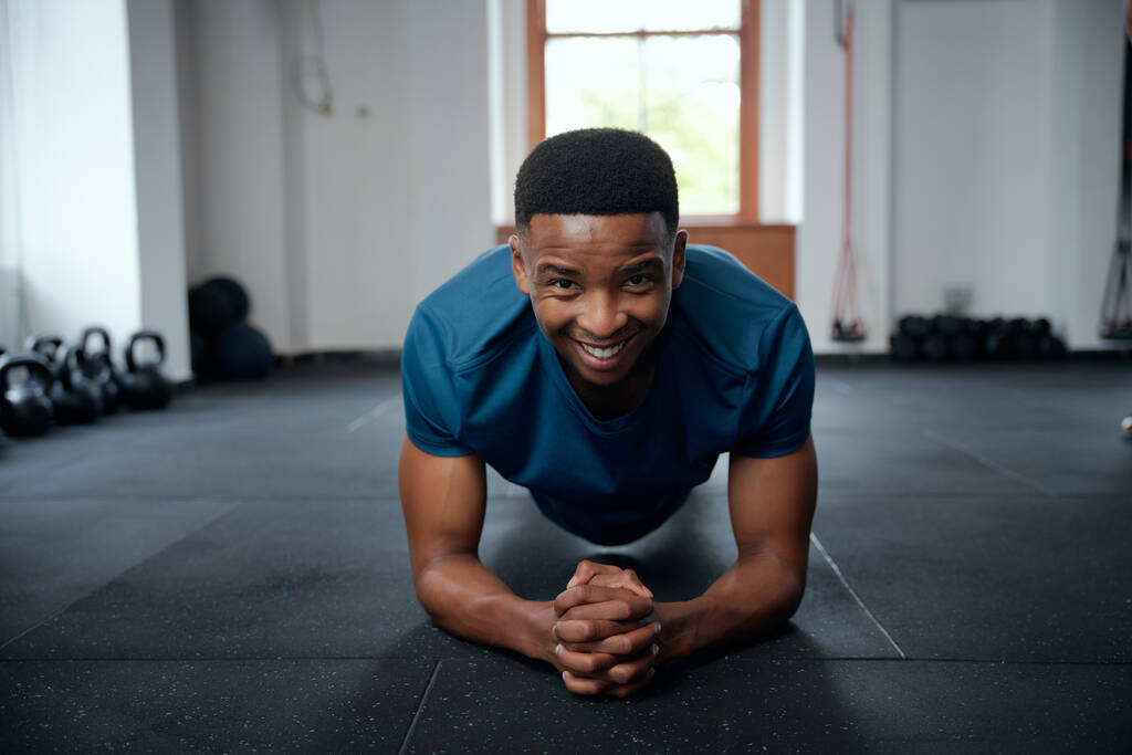 Retrato de un joven negro confiado en ropa deportiva haciendo ejercicios de tablón en el gimnasio - Foto, Imagen
