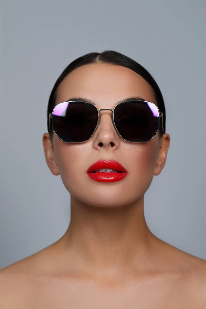 Attraktive Frau mit modischer Sonnenbrille vor grauem Hintergrund - Foto, Bild