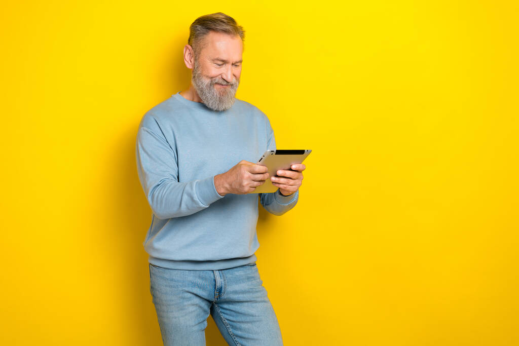 Φωτογραφία από καλή διάθεση συνταξιούχος τύπος φορούν μπλε πουλόβερ ανάγνωση σύγχρονο gadget κενό χώρο απομονωμένο κίτρινο χρώμα φόντο. - Φωτογραφία, εικόνα