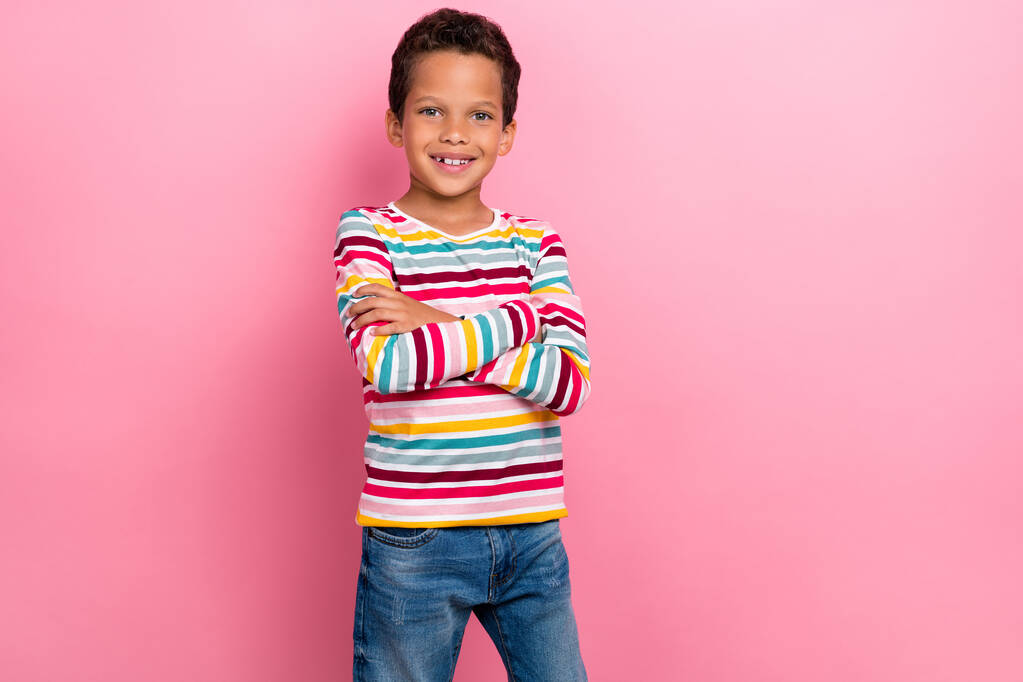 Fénykép aranyos bájos iskolás fiú göndör frizura öltözött csíkos hosszú ujjú karok keresztbe állni elszigetelt rózsaszín színű háttér. - Fotó, kép