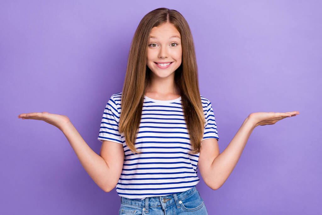 Фото позитивной веселой девушки в полосатой футболке сравнить продукты, демонстрирующие пустое пространство изолированы на фиолетовом фоне цвета. - Фото, изображение
