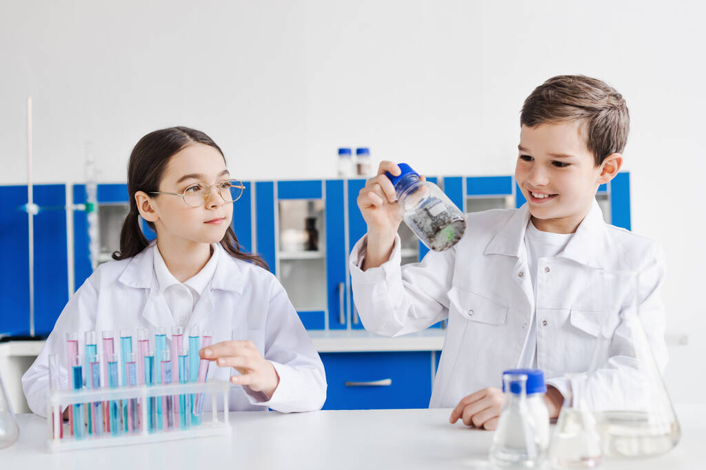 iloinen poika tilalla purkki kemiallisen aineen lähellä tyttö silmälasit ja koeputket laboratoriossa - Valokuva, kuva