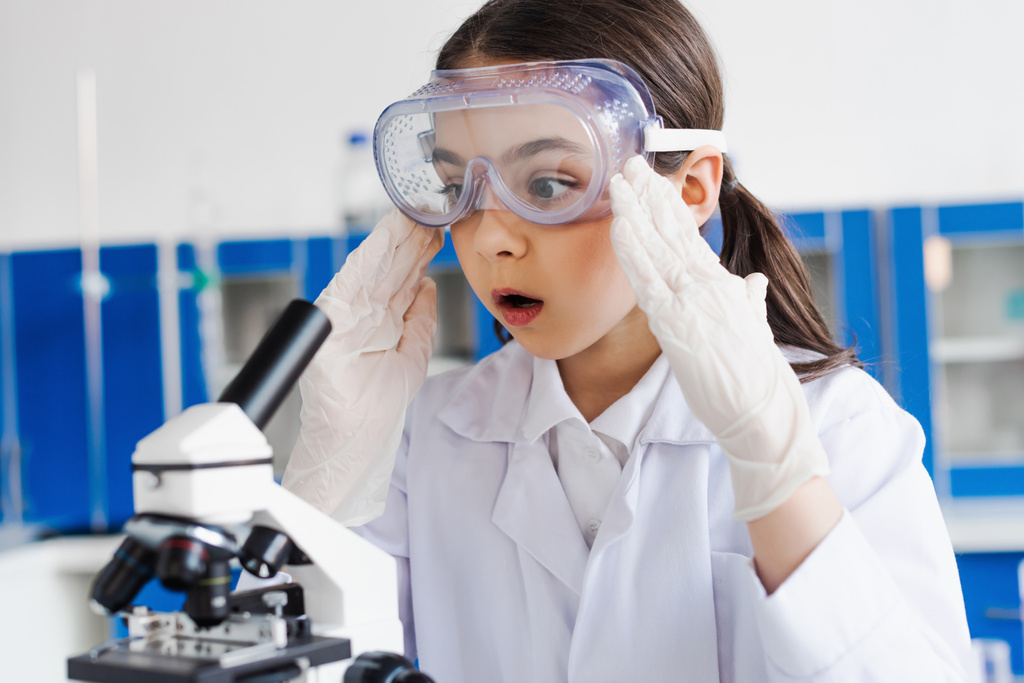 chica impactada en gafas y guantes de látex tocando la cabeza cerca del microscopio en el laboratorio - Foto, imagen