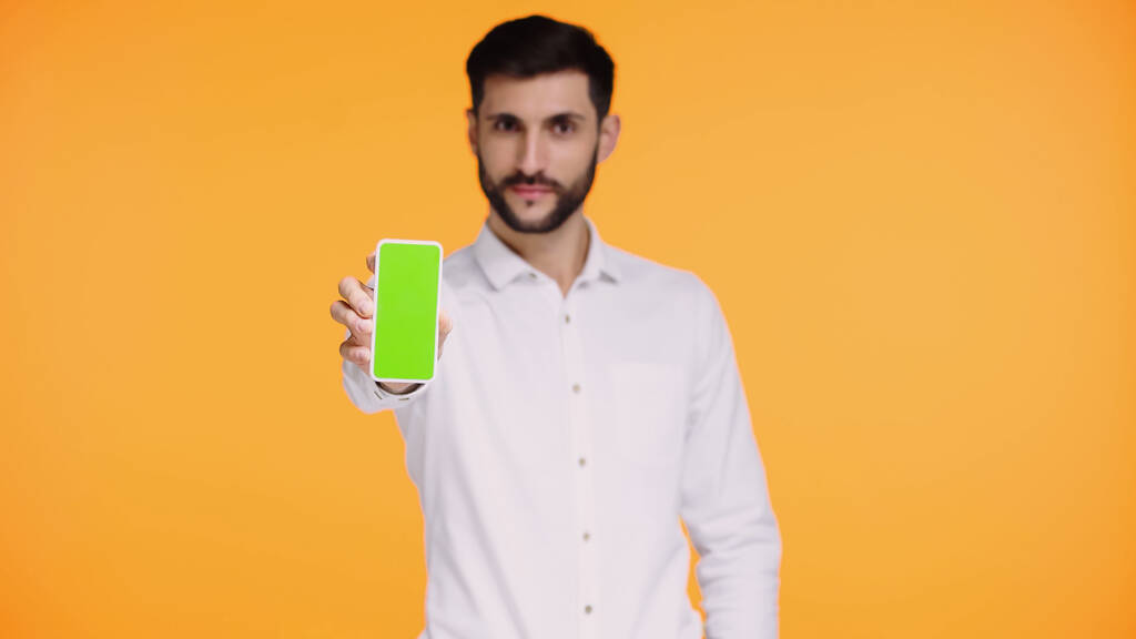 hombre barbudo en camisa blanca sosteniendo teléfono inteligente con pantalla verde aislado en amarillo - Foto, Imagen