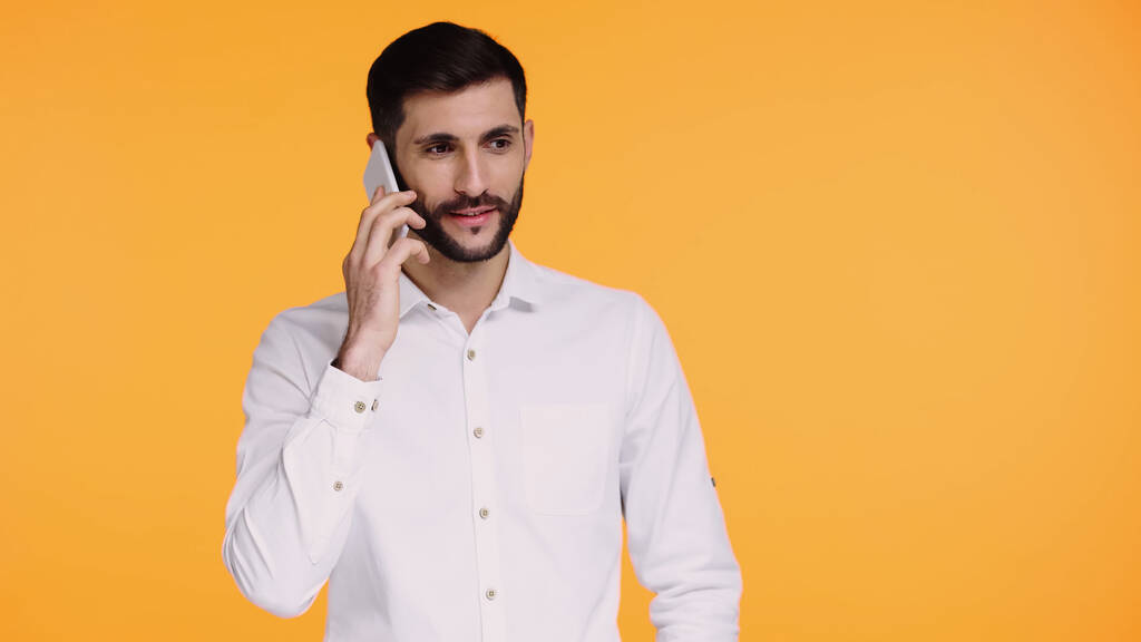 Beyaz gömlekli sakallı adam sarıda izole bir şekilde akıllı telefondan konuşuyor. - Fotoğraf, Görsel