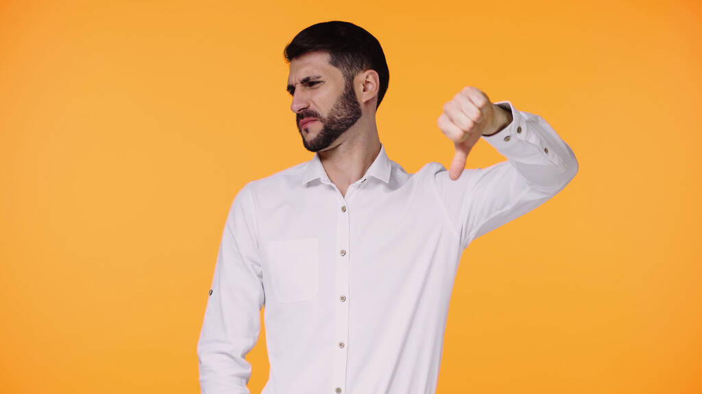 displeased man in white shirt showing dislike gesture isolated on yellow - Photo, Image