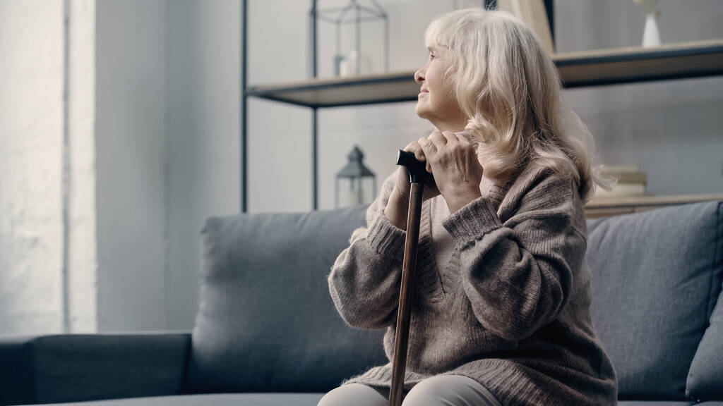 mujer mayor con demencia sentada en un sofá con bastón  - Foto, Imagen
