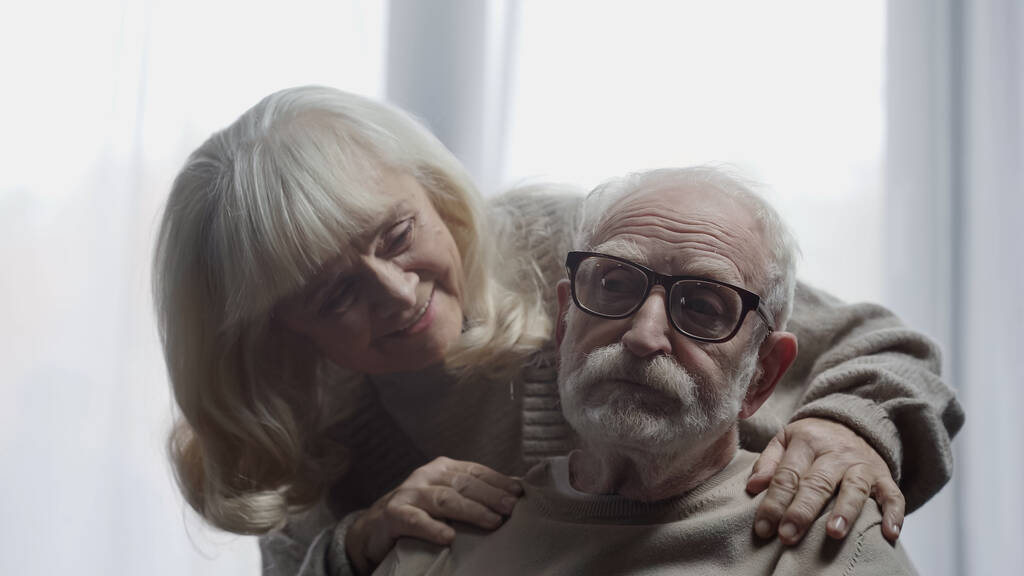 vrolijke senior vrouw kalmeren man in bril met dementie  - Foto, afbeelding