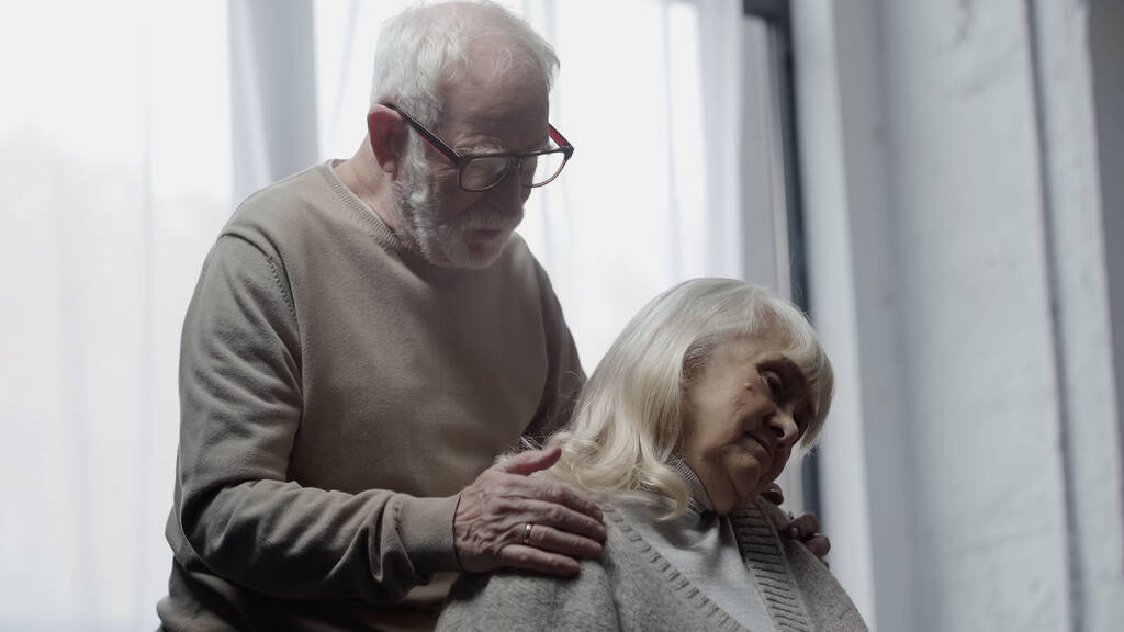 Oudere man in bril kalmeert overstuur vrouw met dementie  - Foto, afbeelding
