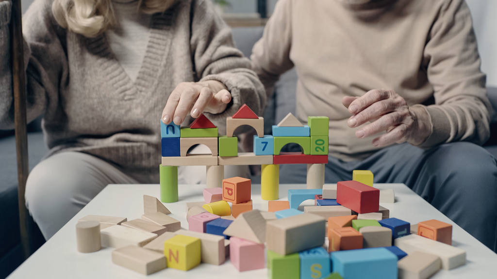 обрізаний вид на старшу пару з деменцією, що грає з барвистими будівельними блоками на столі
  - Фото, зображення