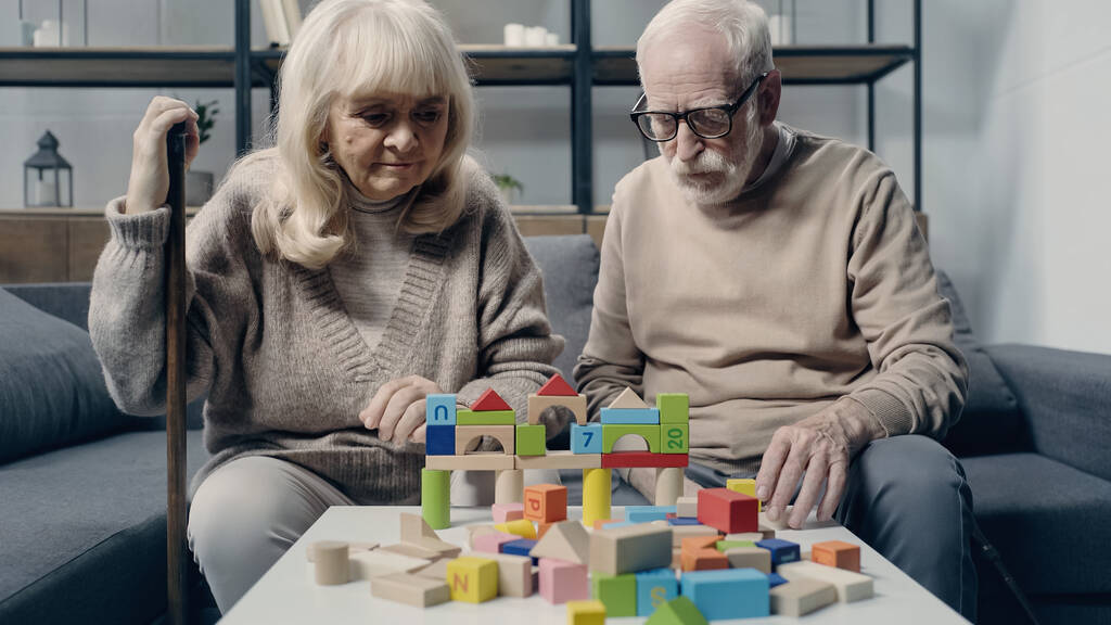 Pareja mayor con demencia jugando con bloques de construcción coloridos en la mesa  - Foto, Imagen