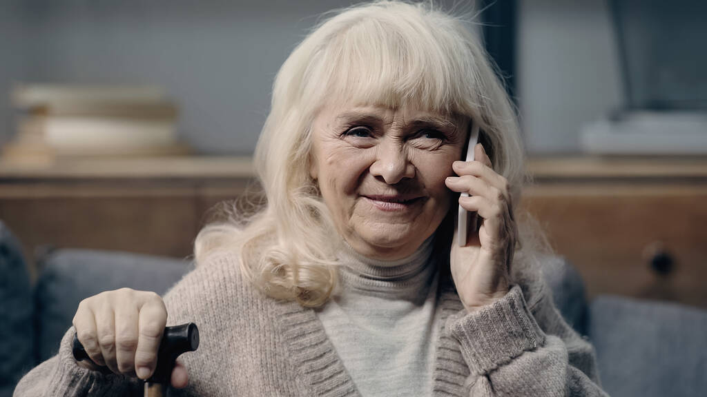 счастливая пожилая женщина с тростью, говорящая по смартфону - Фото, изображение
