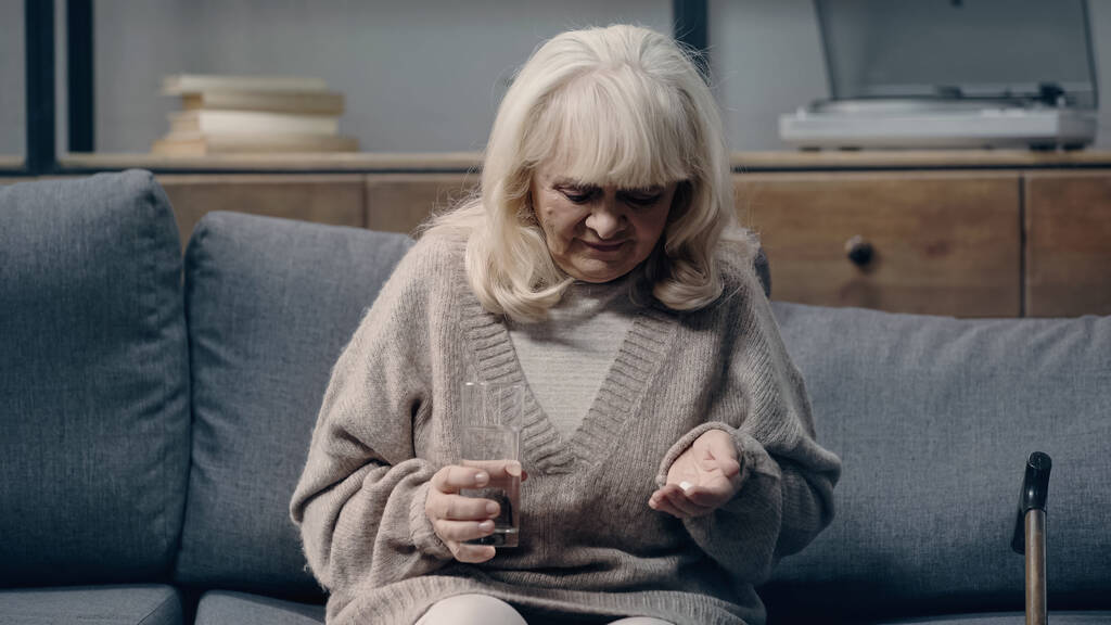 сумна старша жінка з деменцією тримає таблетки і склянку води
 - Фото, зображення