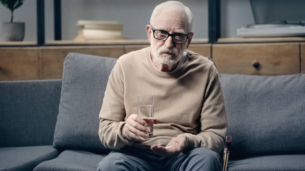 Senior man with dementia holding pills and glass of water  - Photo, Image
