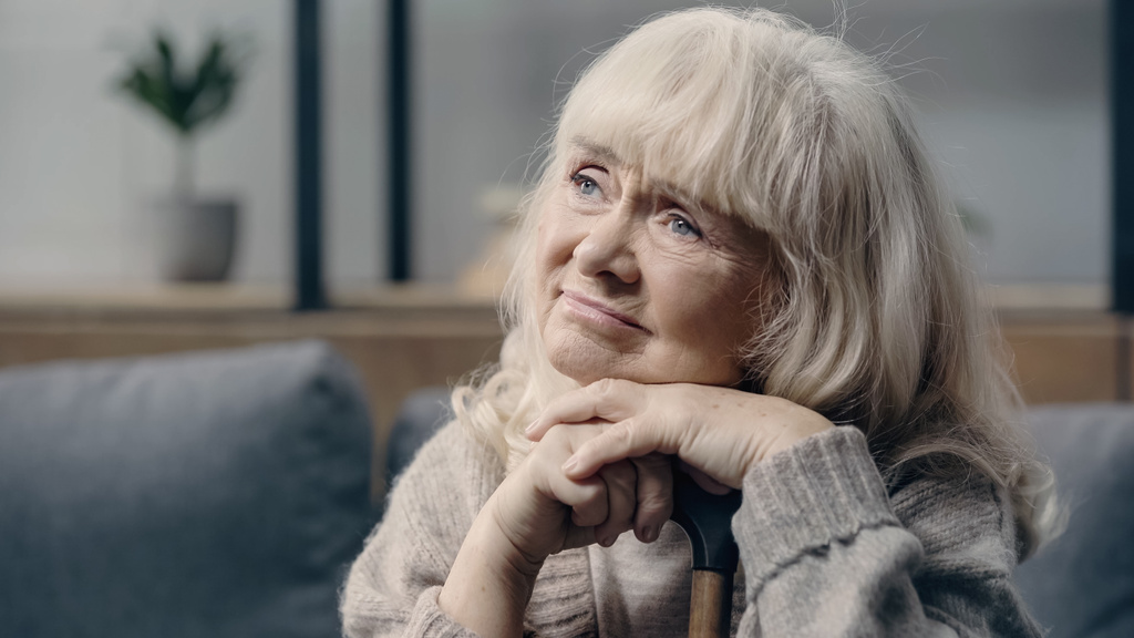 zamyšlená seniorka s demencí sedící doma s vycházkovou holí  - Fotografie, Obrázek