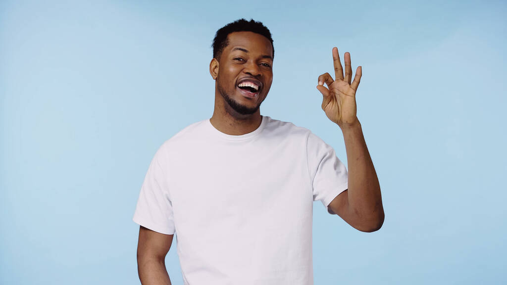 homem americano africano alegre na t-shirt branca que mostra o sinal aprovado isolado no azul - Foto, Imagem