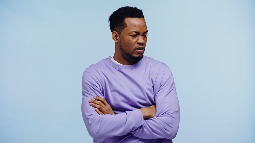 offended african american man in purple pullover standing with crossed arms isolated on blue - Photo, Image