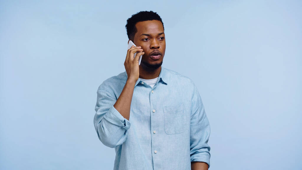 africký Američan v košili mluví na mobilním telefonu izolované na modré - Fotografie, Obrázek