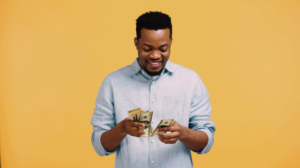 Mutlu Afro-Amerikalı adam sarıda izole edilmiş dolarları sayıyor. - Fotoğraf, Görsel
