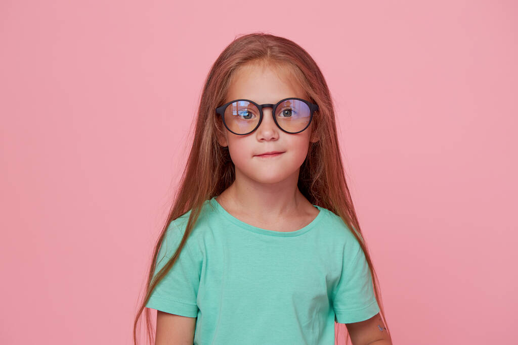 Portrait of cute toddler girl child bespectacled over pink background. Advertising childrens products. Funny face - Foto, Imagem