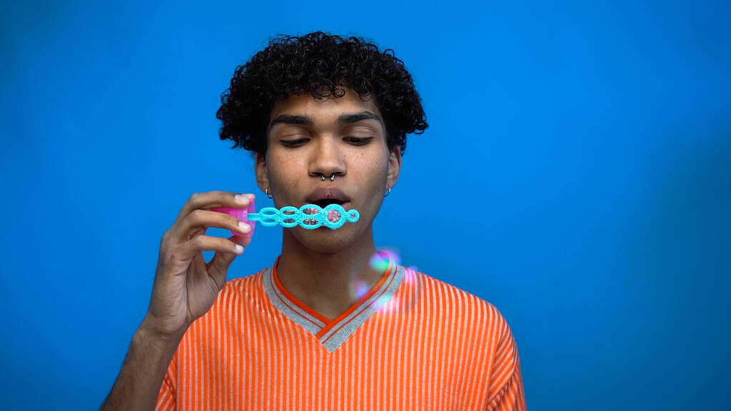 Junger afrikanisch-amerikanischer Mann bläst Seifenblasen isoliert auf blau  - Foto, Bild