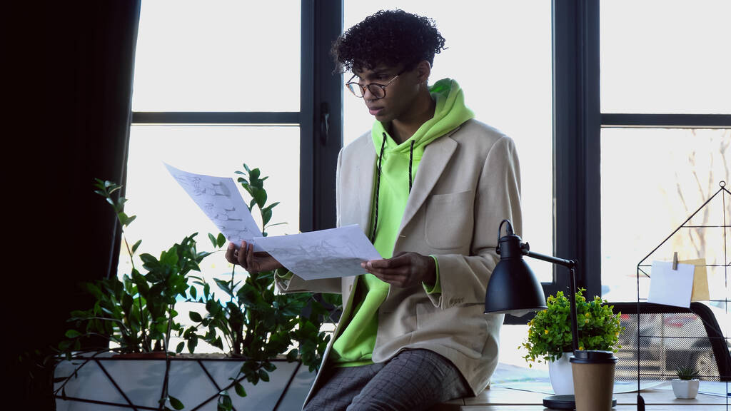 Jovem designer afro-americano segurando esboços em estúdio  - Foto, Imagem