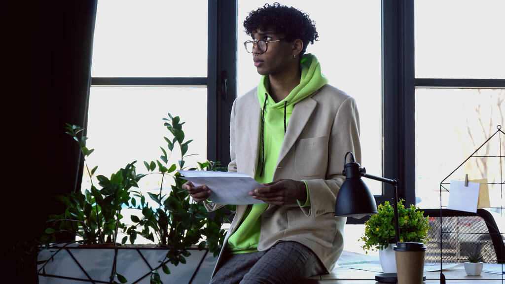 Молодий афроамериканський дизайнер в окулярах тримає ескізи в студії
  - Фото, зображення