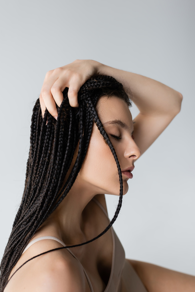 Saçları örgülü ve spor sutyenli genç bir kadın gri renkte izole edilmiş.  - Fotoğraf, Görsel