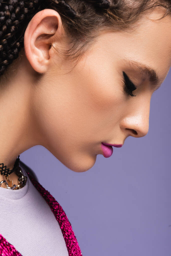 vue latérale de la femme avec maquillage et colliers isolés sur violet - Photo, image