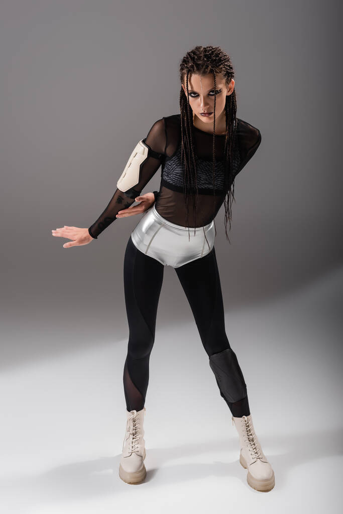 volledige lengte van futuristische vrouw in zwarte bodycon jumpsuit en zilveren shorts op grijze achtergrond - Foto, afbeelding