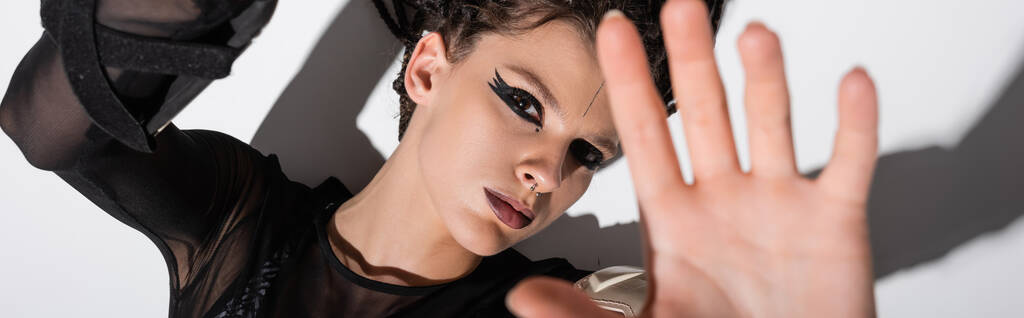 vista superior da mulher com maquiagem expressiva e mão estendida olhando para a câmera no fundo branco com sombra, banner - Foto, Imagem