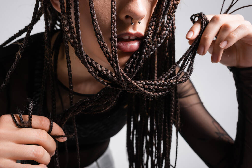 περικοπή άποψη της γυναίκας με σκουλαρίκια αγγίγματα πλεγμένα dreadlocks απομονώνονται σε γκρι - Φωτογραφία, εικόνα