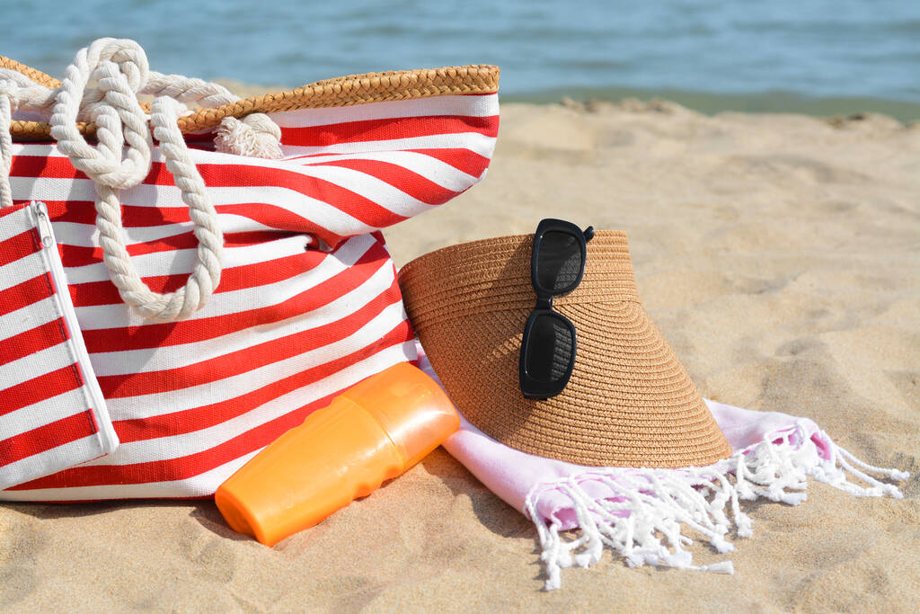 Stylish striped bag with beach accessories on sand near sea - Zdjęcie, obraz