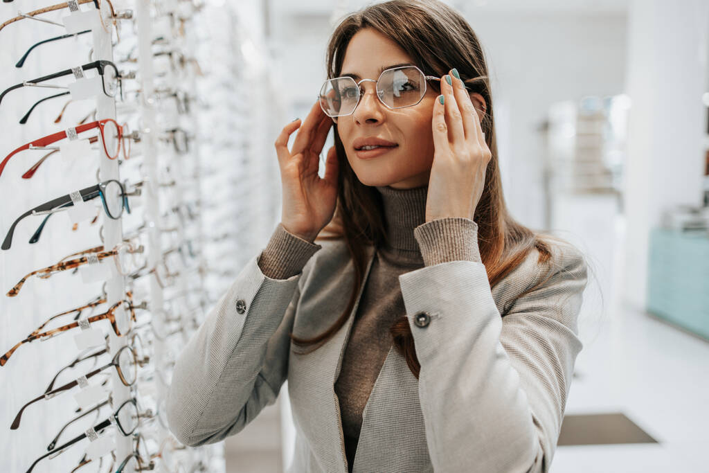 Mooie en modieuze vrouw kiezen bril frame in moderne optische winkel. - Foto, afbeelding