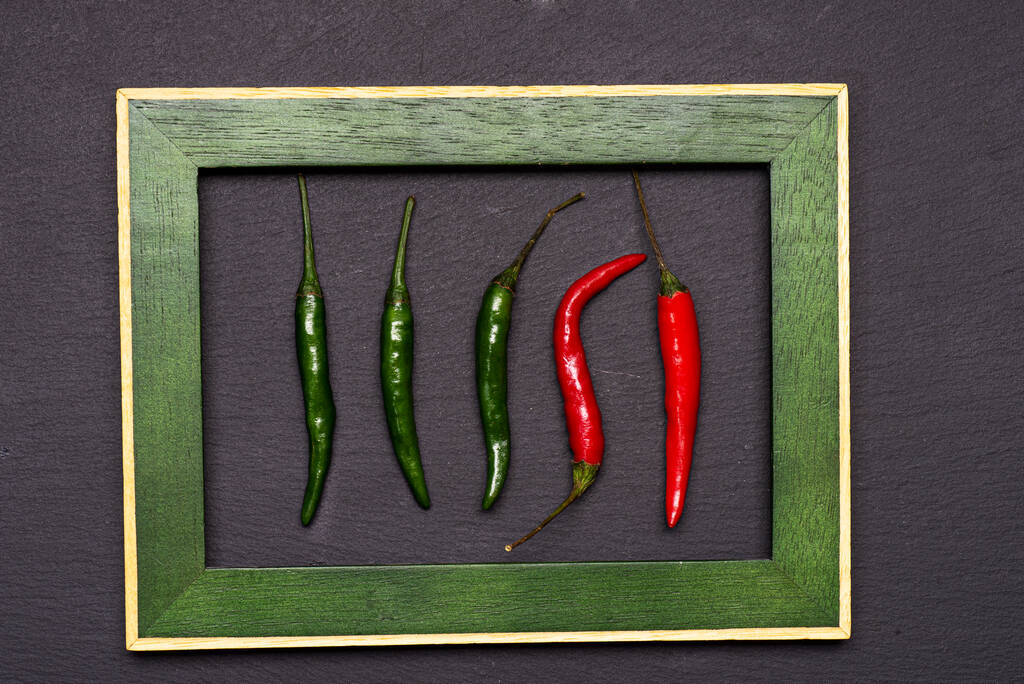 Rot und Grün: ein würziges Paar frischer Chilischoten vor schwarzem Hintergrund in einem Porträtrahmen. Ansicht der Tischplatte, flache Lage, Kopierraum. - Foto, Bild