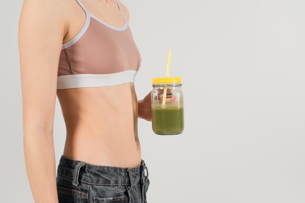 oříznutý pohled na fit žena ve sportovní top drží čerstvý smoothie izolované na šedé - Fotografie, Obrázek