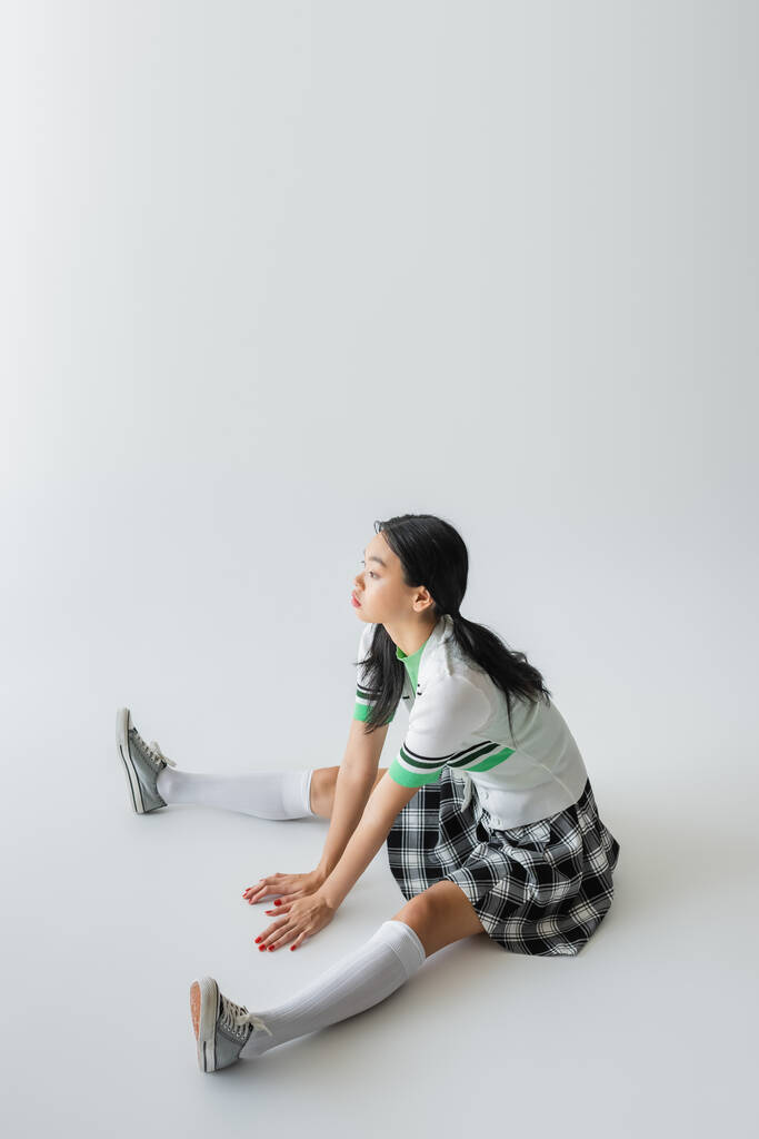 Stílusos ázsiai nő szoknya és térd zokni ül szürke háttér  - Fotó, kép
