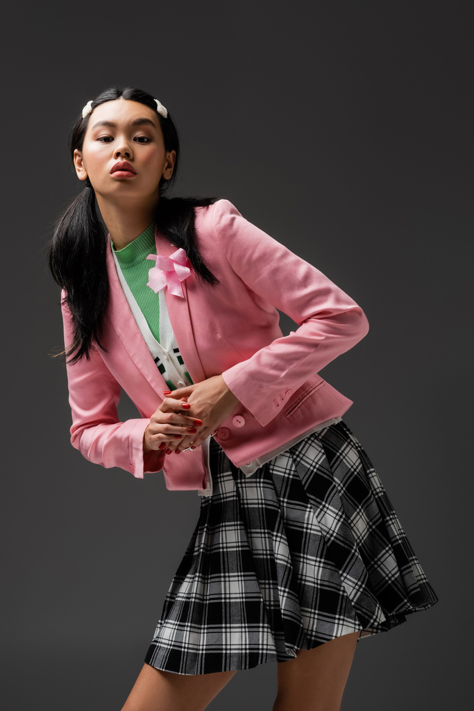 Pretty asian woman in skirt and pink jacket looking at camera isolated on grey  - Photo, Image