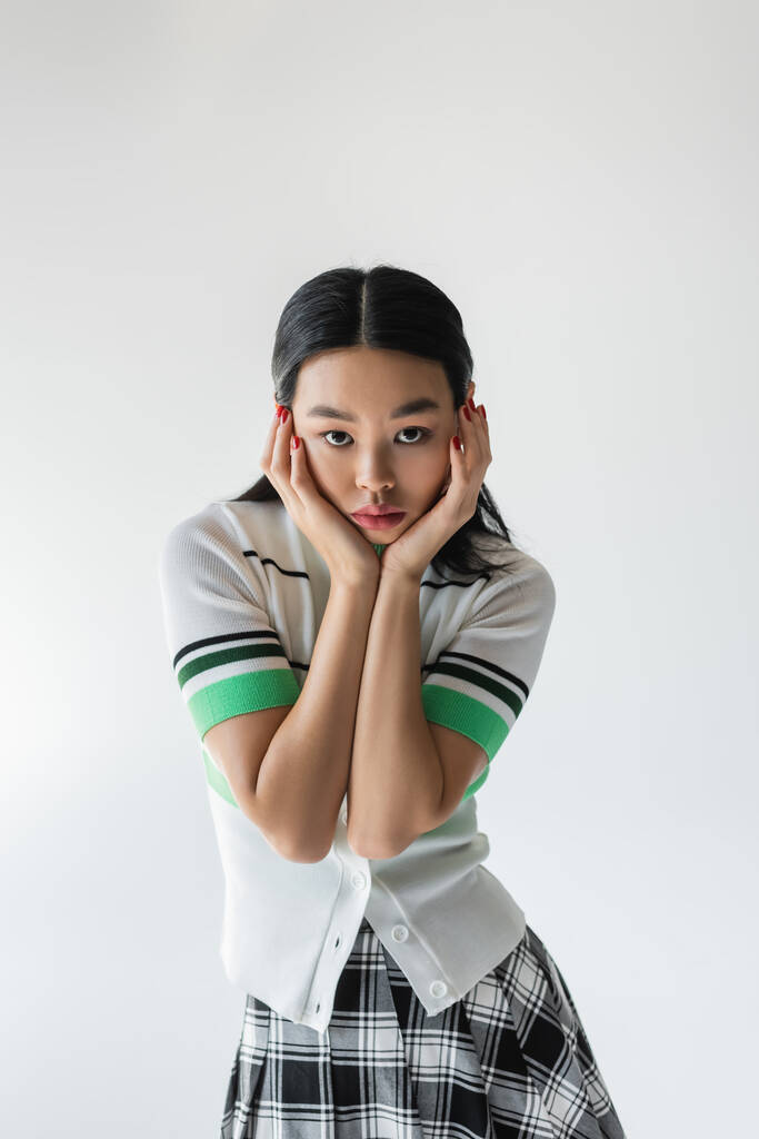 Moda modelo asiático em cardigan cortado tocando rosto isolado em cinza  - Foto, Imagem