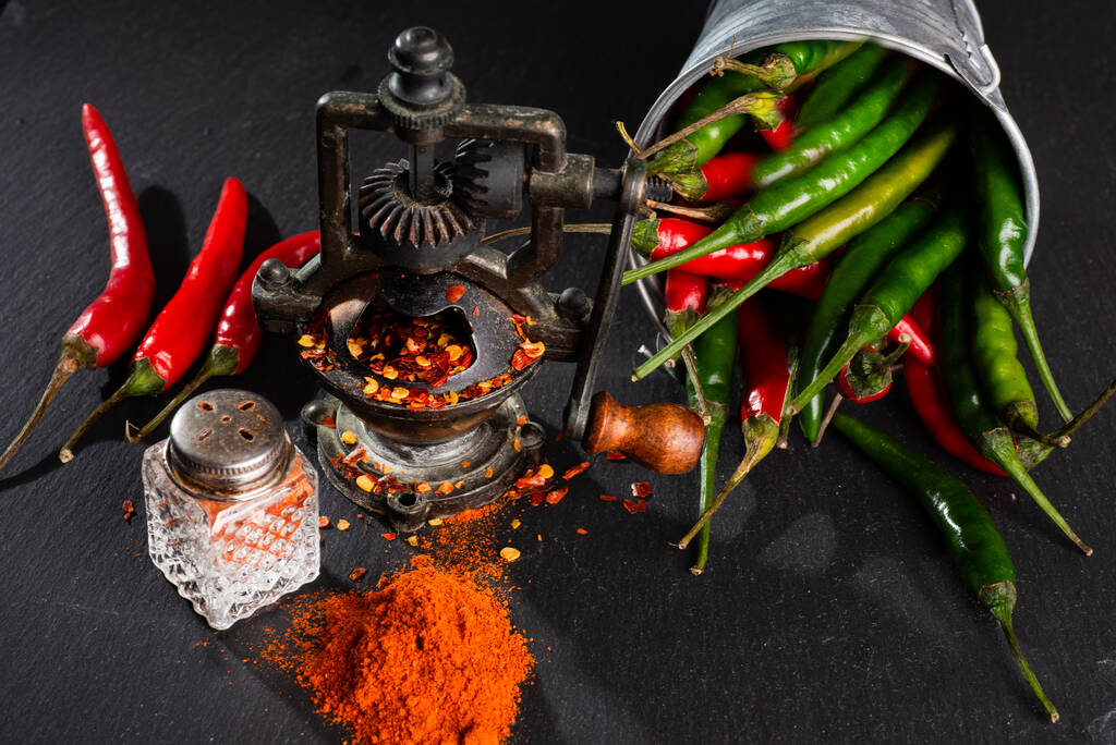mill and finely ground red hot pepper, pepper pods on a black table. - Photo, Image