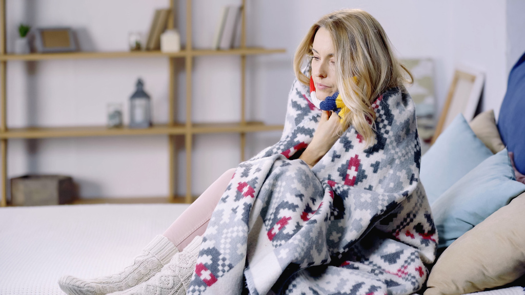 donna malata e triste seduta sul letto sotto coperta colorata  - Foto, immagini