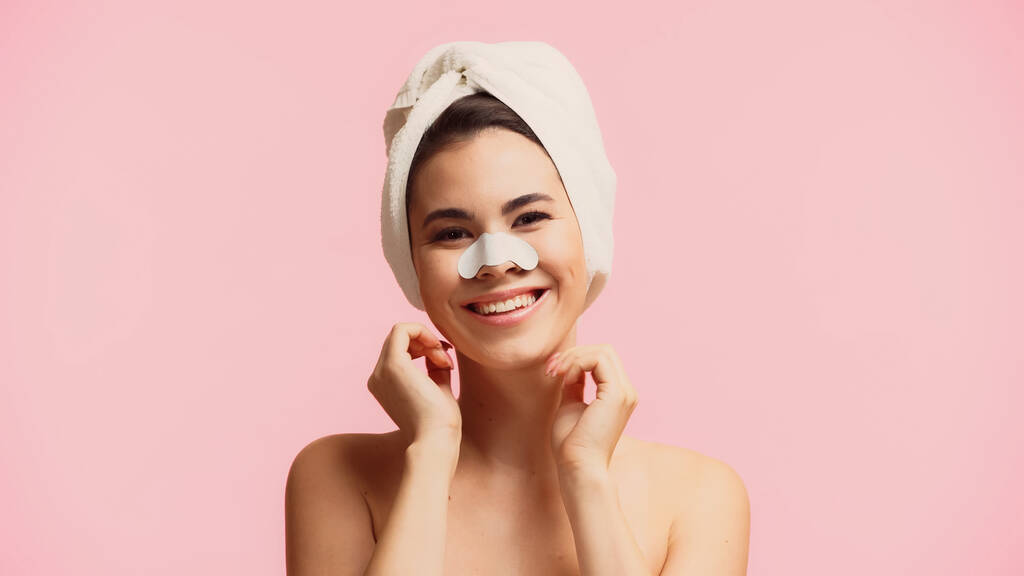 Χαρούμενη νεαρή γυναίκα με πετσέτα στο κεφάλι και μπάλωμα στη μύτη χαμογελώντας απομονωμένη στο ροζ - Φωτογραφία, εικόνα