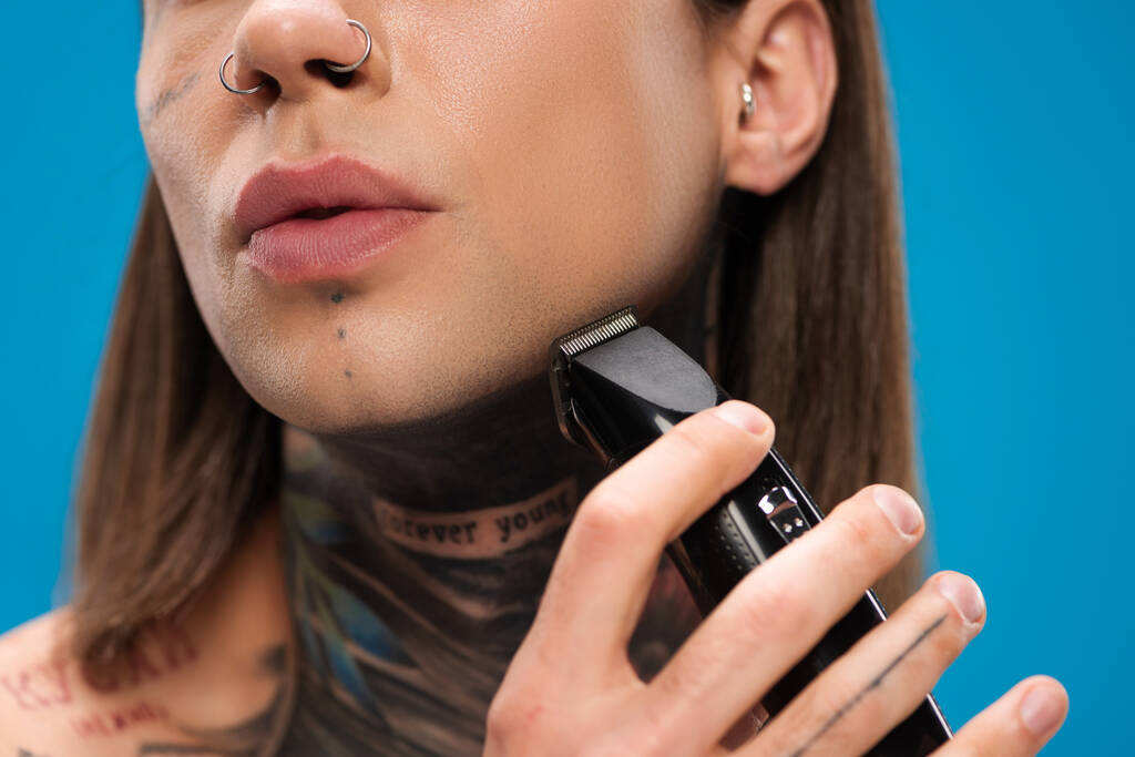 cropped view of young and tattooed man shaving with electric razor isolated on blue - Photo, Image