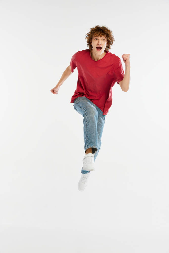 Front camera view of excited young man running isolated over white background. Sport, dance, fitness, happiness. Model in casual style clothes in motion at studio shoot - Photo, Image
