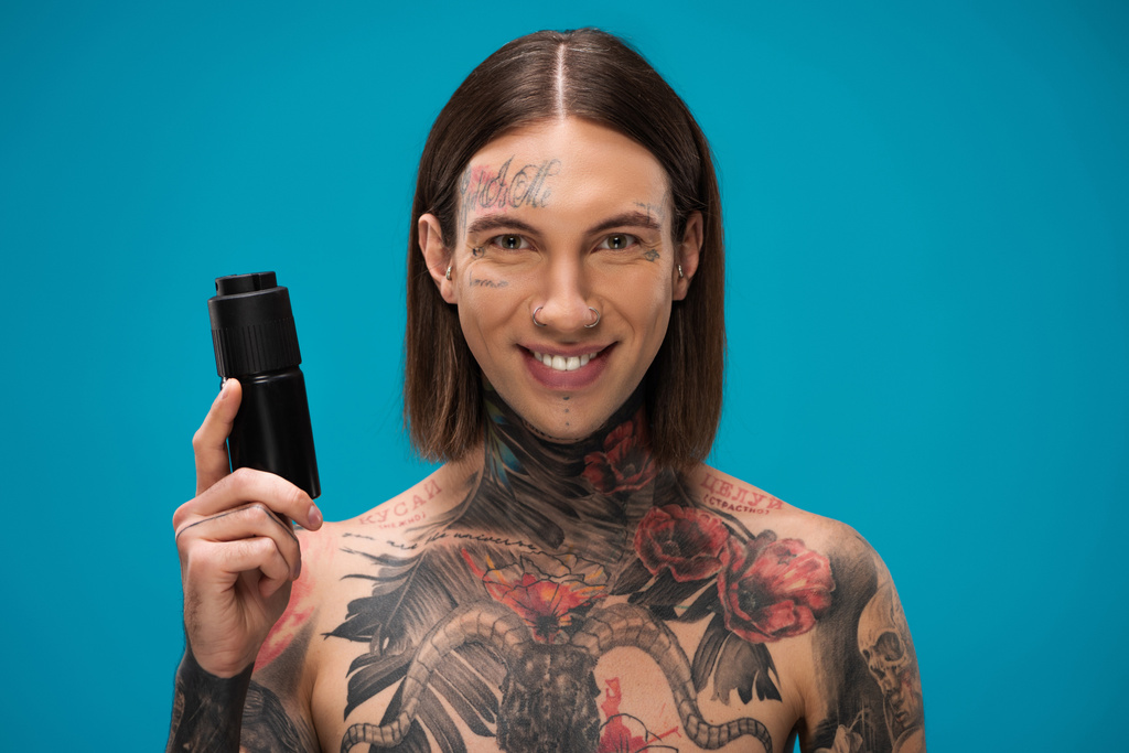 felice e tatuato giovane uomo tenendo antitraspirante isolato su blu - Foto, immagini